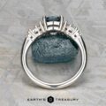 The "Tigrina" ring in platinum with a 1.25-carat Montana sapphire is displayed upright, highlighting its setting and band, against a blue stone background with the "Earth's Treasury" logo below.