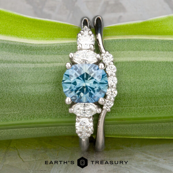 The "Tigrina" ring in platinum with 1.25-carat Montana sapphire, alongside the "Electra" band in platinum The "Tigrina" ring in platinum with a 1.25-carat Montana sapphire and the "Electra" band in platinum are displayed together on a green leaf.