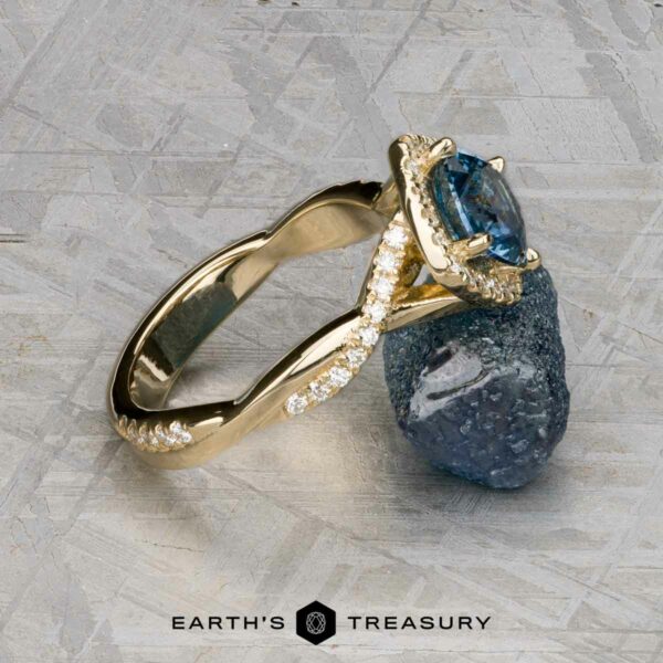 The "Yvette" ring in 14k yellow gold with 1.64-carat Montana sapphire The "Yvette" ring in 14k yellow gold, featuring a 1.64-carat Montana sapphire, rests against a rough stone on a textured surface. The Earth's Treasury logo is displayed at the bottom.