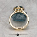 The "Yvette" ring in 14k yellow gold with a 1.64-carat Montana sapphire is shown upright on a rough blue stone, with the Earth's Treasury logo below.