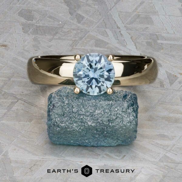 The "Davina" ring in 14k yellow gold with 1.43-carat Montana sapphire The "Davina" ring in 14k yellow gold with a 1.43-carat Montana sapphire sits atop a rough blue stone, against a textured gray background. Logo text at bottom reads "Earth's Treasury.