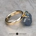 The "Davina" ring in 14k yellow gold with a 1.43-carat Montana sapphire is displayed leaning against a rough stone on a textured surface, with the Earth's Treasury logo below.