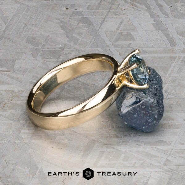 The "Davina" ring in 14k yellow gold with 1.43-carat Montana sapphire The "Davina" ring in 14k yellow gold with a 1.43-carat Montana sapphire is displayed leaning against a rough stone on a textured surface, with the Earth's Treasury logo below.