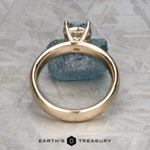 The "Davina" ring in 14k yellow gold, featuring a 1.43-carat Montana sapphire, is displayed upright on a textured gray surface with the Earth's Treasury logo below.