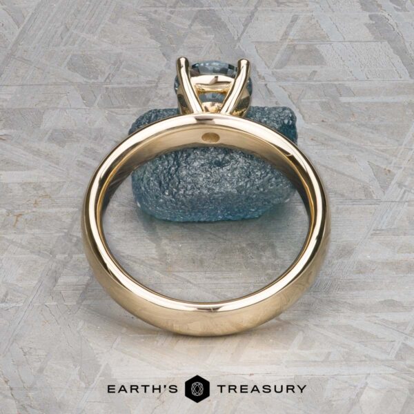 The "Davina" ring in 14k yellow gold with 1.43-carat Montana sapphire The "Davina" ring in 14k yellow gold, featuring a 1.43-carat Montana sapphire, is displayed upright on a textured gray surface with the Earth's Treasury logo below.