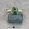 The "Blythe" ring in 14k yellow gold features a 1.51-carat green sapphire and small side diamonds, displayed on a rough blue-green crystal with the "Earth's Treasury" logo below.