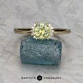 The "Wren" ring in 14k yellow gold with a 0.91-carat Montana sapphire is displayed on a rough blue crystal, with "Earth’s Treasury" logo and text at the bottom.