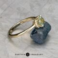 The "Wren" ring in 14k yellow gold, featuring a 0.91-carat Montana sapphire and small diamonds, is shown resting on a rough dark mineral with the Earth's Treasury logo below.