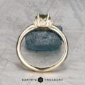 The "Wren" ring in 14k yellow gold features a 0.91-carat Montana sapphire in a pronged setting with a small white diamond, displayed upright on rough blue stone. The "Earth's Treasury" logo is shown at the bottom.