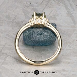 The "Wren" ring in 14k yellow gold features a 0.91-carat Montana sapphire in a pronged setting with a small white diamond, displayed upright on rough blue stone. The "Earth's Treasury" logo is shown at the bottom.
