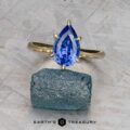 The Cathedral "Anemone" ring in 14K yellow gold with a 2.37-carat Ceylon sapphire is displayed upright on a rough blue stone, with the "Earth's Treasury" logo and text below.