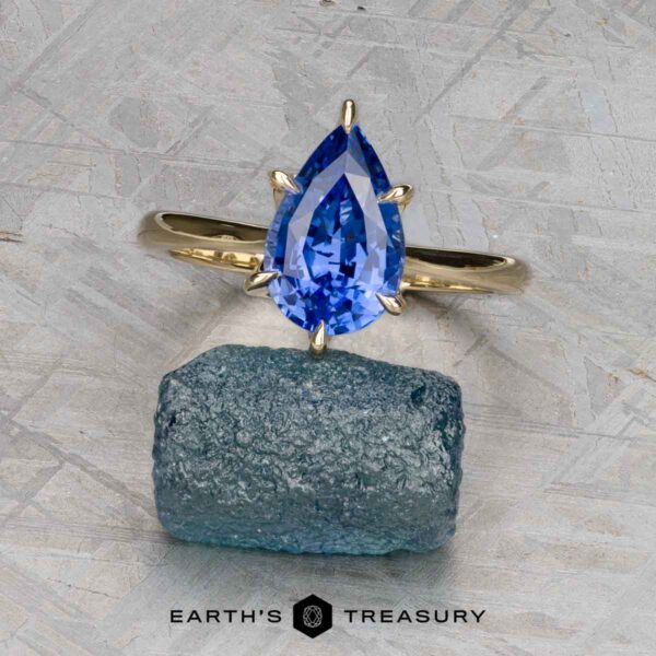 The Cathedral "Anemone" ring in 14K yellow gold with 2.37-carat Ceylon sapphire The Cathedral "Anemone" ring in 14K yellow gold with a 2.37-carat Ceylon sapphire is displayed upright on a rough blue stone, with the "Earth's Treasury" logo and text below.