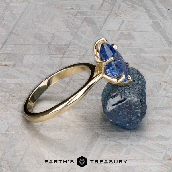The Cathedral "Anemone" ring in 14K yellow gold with 2.37-carat Ceylon sapphire The Cathedral "Anemone" ring in 14K yellow gold with a 2.37-carat Ceylon sapphire is displayed upright on a rough blue stone, with the "Earth's Treasury" logo and text below.