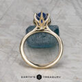 The Cathedral "Anemone" ring in 14K yellow gold with a 2.37-carat Ceylon sapphire is displayed upright on a rough blue stone, with the "Earth's Treasury" logo and text below.