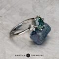The "Xena" ring in platinum, featuring a 2.27-carat Australian sapphire, is displayed on a rough blue mineral with the "Earth's Treasury" logo below.