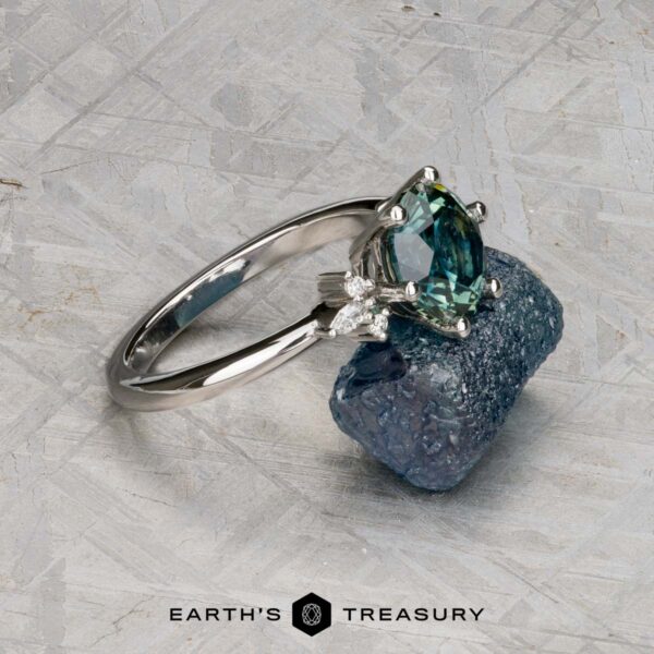 The "Xena" ring in platinum with 2.27-carat Australian sapphire The "Xena" ring in platinum, featuring a 2.27-carat Australian sapphire, is displayed on a rough blue mineral with the "Earth's Treasury" logo below.