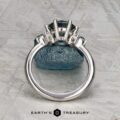 The "Xena" ring in platinum with a 2.27-carat Australian sapphire stands upright on a rough blue stone, photographed on a textured grey surface with the "Earth's Treasury" logo at the bottom.