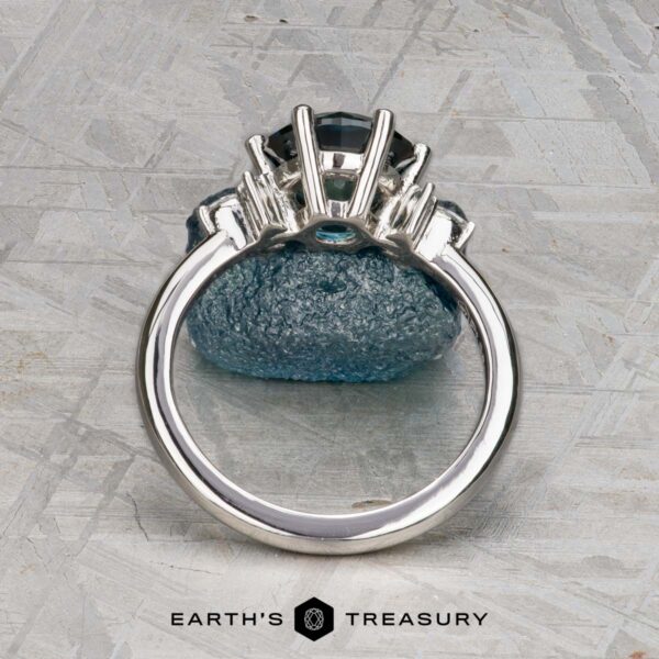The "Xena" ring in platinum with 2.27-carat Australian sapphire The "Xena" ring in platinum with a 2.27-carat Australian sapphire stands upright on a rough blue stone, photographed on a textured grey surface with the "Earth's Treasury" logo at the bottom.