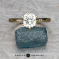 The "Carmen" ring in 14k yellow gold, featuring a 1.29-carat Montana sapphire and small side diamonds, is displayed on a rough blue stone with "Earth's Treasury" written below.