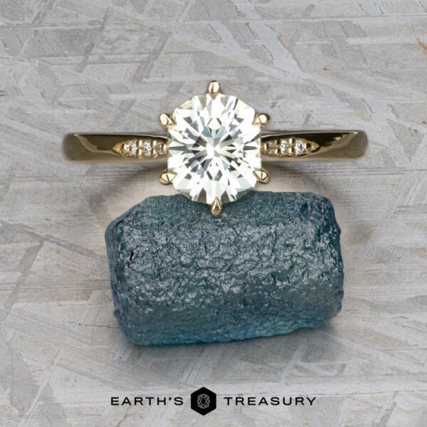 The "Carmen" ring in 14k yellow gold with 1.29-carat Montana sapphire The "Carmen" ring in 14k yellow gold, featuring a 1.29-carat Montana sapphire and small side diamonds, is displayed on a rough blue stone with "Earth's Treasury" written below.