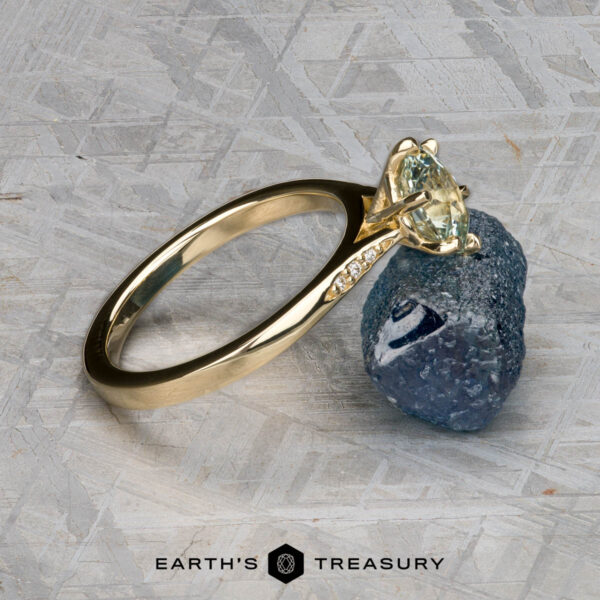 The "Carmen" ring in 14k yellow gold with 1.29-carat Montana sapphire The "Carmen" ring in 14k yellow gold featuring a 1.29-carat Montana sapphire and accent stones rests on a rough blue stone, with the Earth's Treasury logo at the bottom.