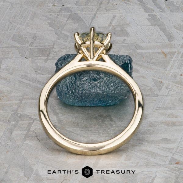 The "Carmen" ring in 14k yellow gold with 1.29-carat Montana sapphire The "Carmen" ring in 14k yellow gold with a 1.29-carat Montana sapphire stands upright on a textured blue stone, set against a patterned gray background. The Earth's Treasury logo is visible below.