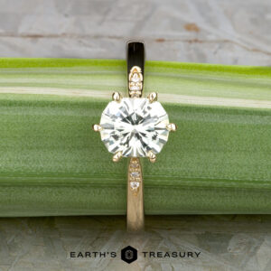 The "Carmen" ring in 14k yellow gold, featuring a 1.29-carat Montana sapphire center stone and accent gems on the band, is displayed on a green leaf with the Earth’s Treasury logo below.