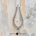 The "Nigella" ring keeper necklace in 14K white gold hangs on a chain against a textured, neutral-toned background. Text at the bottom reads "EARTH'S TREASURY.