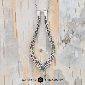 The "Nigella" ring keeper necklace in 14K white gold hangs on a chain against a textured, neutral-toned background. Text at the bottom reads "EARTH'S TREASURY.