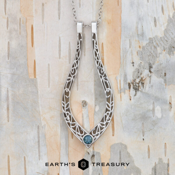 The "Nigella" ring keeper necklace in 14K white gold The "Nigella" ring keeper necklace in 14K white gold hangs on a chain against a textured, neutral-toned background. Text at the bottom reads "EARTH'S TREASURY.