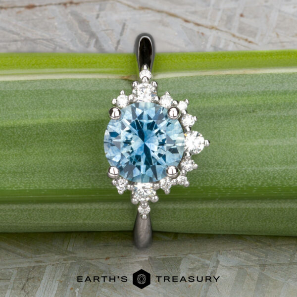 The "Veronica" ring in 14k white gold with 1.53-carat Montana sapphire The "Veronica" ring in 14k white gold, featuring a 1.53-carat Montana sapphire surrounded by small white stones, is displayed on a green leaf background.