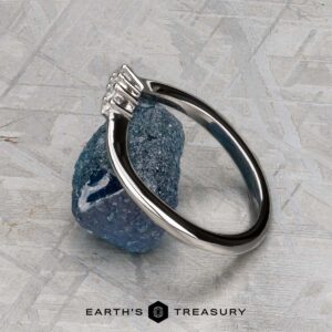The "Veronica" band in 14k white gold, featuring a geometric design, is displayed on a rough blue gemstone, with the "EARTH'S TREASURY" logo and text below.