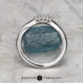The "Veronica" band in 14k white gold with four diamonds stands upright before a blue rough gemstone on a textured gray surface. The Earth’s Treasury logo appears at the bottom.