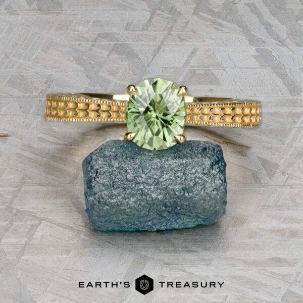 The "Maya" ring in 18k yellow gold with 1.48-carat Australian sapphire The "Maya" ring in 18k yellow gold, set with a 1.48-carat Australian sapphire, is displayed balanced on a raw blue-green crystal against a textured gray background.