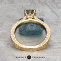 The "Maya" ring in 18k yellow gold features ornate engravings and a 1.48-carat Australian sapphire, shown upright on a textured surface with a blue stone in the background.