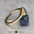 The "Maeve" ring in 14k yellow gold with a 0.91-carat Montana sapphire and a small diamond, displayed on a rough mineral rock, featuring the Earth's Treasury logo at the bottom.