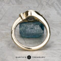 The "Maeve" ring, crafted in 14k yellow gold with a 0.91-carat uncut Montana sapphire, stands upright on a textured gray surface. "EARTH'S TREASURY" is displayed at the bottom of the image.