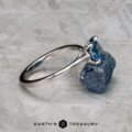 The "Elena" ring in 14k white gold with a 1.93-carat Montana sapphire sits on a rough blue stone atop a textured gray surface, with "EARTH'S TREASURY" displayed at the bottom.