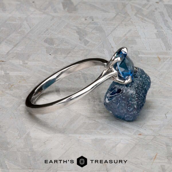 The "Elena" ring in 14k white gold with 1.93-carat Montana sapphire The "Elena" ring in 14k white gold with a 1.93-carat Montana sapphire sits on a rough blue stone atop a textured gray surface, with "EARTH'S TREASURY" displayed at the bottom.