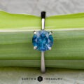 The "Elena" ring in 14k white gold with a 1.93-carat Montana sapphire is shown upright against a green leaf background. The text “EARTH’S TREASURY” appears at the bottom.