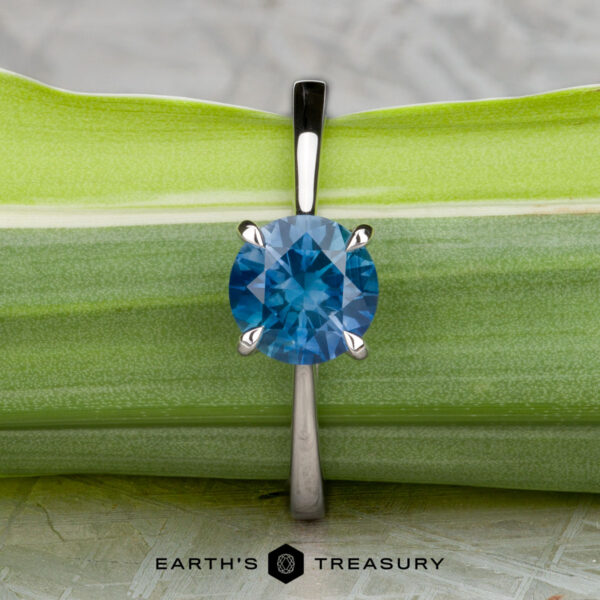 The "Elena" ring in 14k white gold with 1.93-carat Montana sapphire The "Elena" ring in 14k white gold with a 1.93-carat Montana sapphire is shown upright against a green leaf background. The text “EARTH’S TREASURY” appears at the bottom.