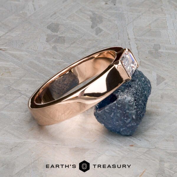 The "Theo" ring in 14k rose gold with 0.48-carat heirloom diamond The "Theo" ring in 14k rose gold with a 0.48-carat heirloom diamond is displayed on a rough blue stone, with the Earth's Treasury logo below.