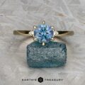 The "Samia" ring in 14k yellow gold, featuring a 1.73-carat Montana sapphire and two small side diamonds, is displayed on a rough blue stone above the Earth's Treasury logo.