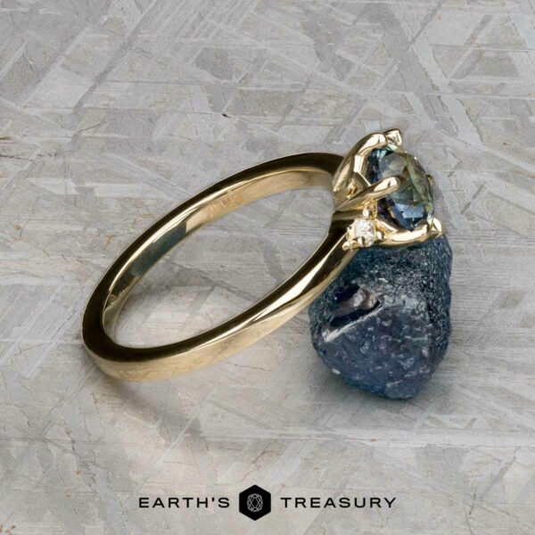 The "Samia" ring in 14k yellow gold with 1.73-carat Montana sapphire The "Samia" ring in 14k yellow gold, featuring a 1.73-carat Montana sapphire, is placed on a rough stone atop a textured surface with the Earth’s Treasury logo at the bottom.