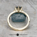 The "Samia" ring in 14k yellow gold, featuring a 1.73-carat Montana sapphire, is displayed vertically on a blue stone surface with a geometric patterned background and the Earth's Treasury logo below.