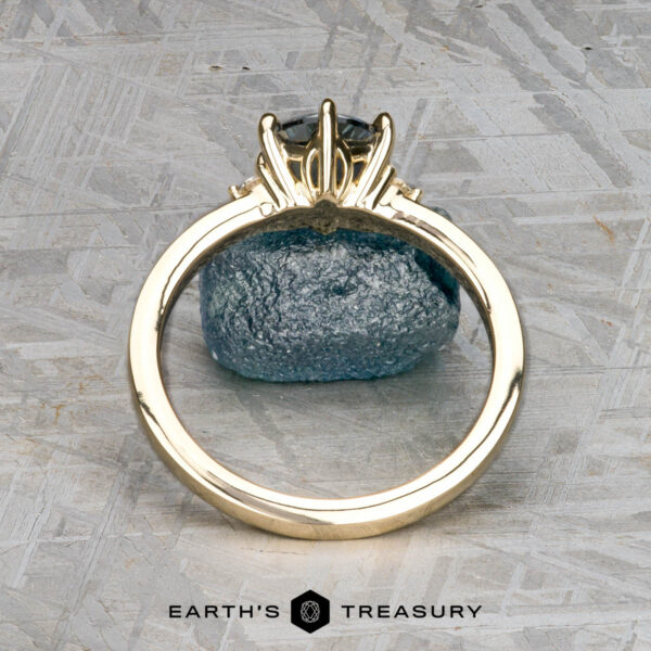 The "Samia" ring in 14k yellow gold with 1.73-carat Montana sapphire The "Samia" ring in 14k yellow gold, featuring a 1.73-carat Montana sapphire, is displayed vertically on a blue stone surface with a geometric patterned background and the Earth's Treasury logo below.