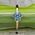 The "Samia" ring in 14k yellow gold features a 1.73-carat Montana sapphire center with two small clear side stones, displayed on a green leaf with the text “Earth’s Treasury” beneath.