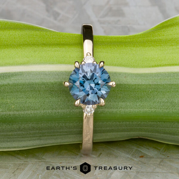 The "Samia" ring in 14k yellow gold with 1.73-carat Montana sapphire The "Samia" ring in 14k yellow gold features a 1.73-carat Montana sapphire center with two small clear side stones, displayed on a green leaf with the text “Earth’s Treasury” beneath.