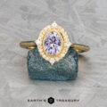 The "Marietta" ring, crafted in 18k yellow gold with a 1.13-carat Montana sapphire and diamond accents, is displayed atop a rough blue-green stone.
