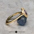 The "Marietta" ring in 18k yellow gold, featuring a 1.13-carat rectangular Montana sapphire, rests on a rough dark stone atop a textured gray surface. The Earth's Treasury logo is shown at the bottom.